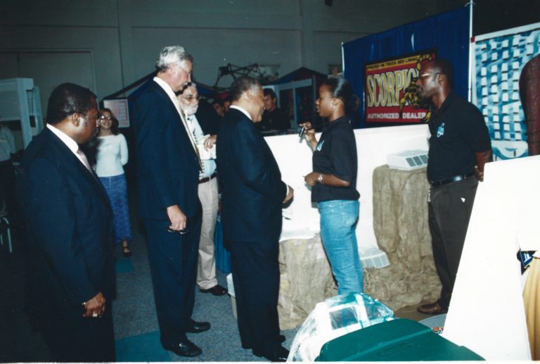 Prime Minister Owen Arthur, our first customer purchasing a Wearable Air Purifier from then medical student Dionne Grannum at BMEX 2003 while Cecil Grannum who managed the booth looks on.